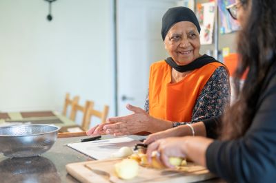 Woman preparing a meal with someone in a kitchen, smiling and gesturing in conversation.